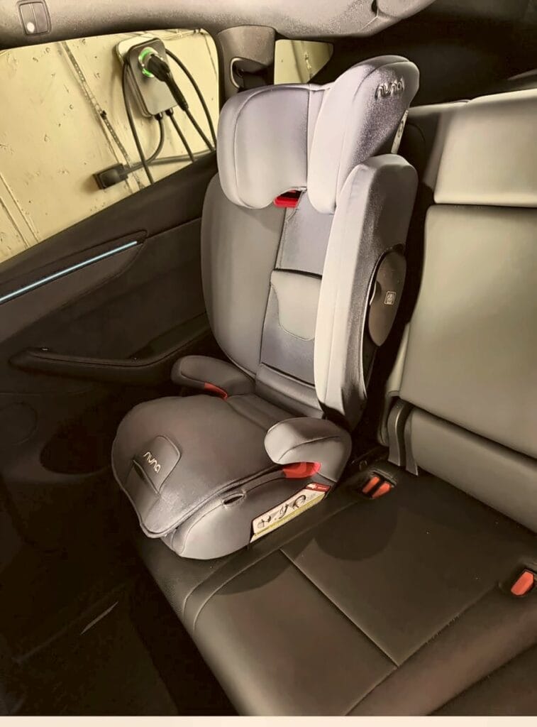 Side view of a Nuna Aace high-back booster against the Tesla Model Y seatback