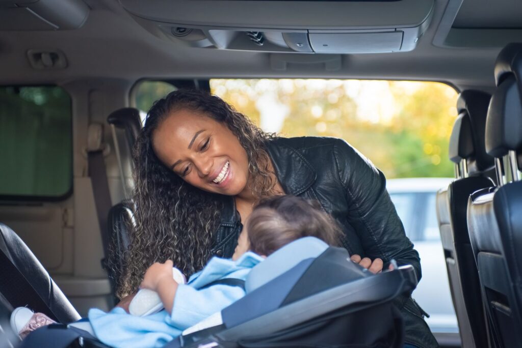 A joyful mother smiles at her baby securely buckled into a car seat