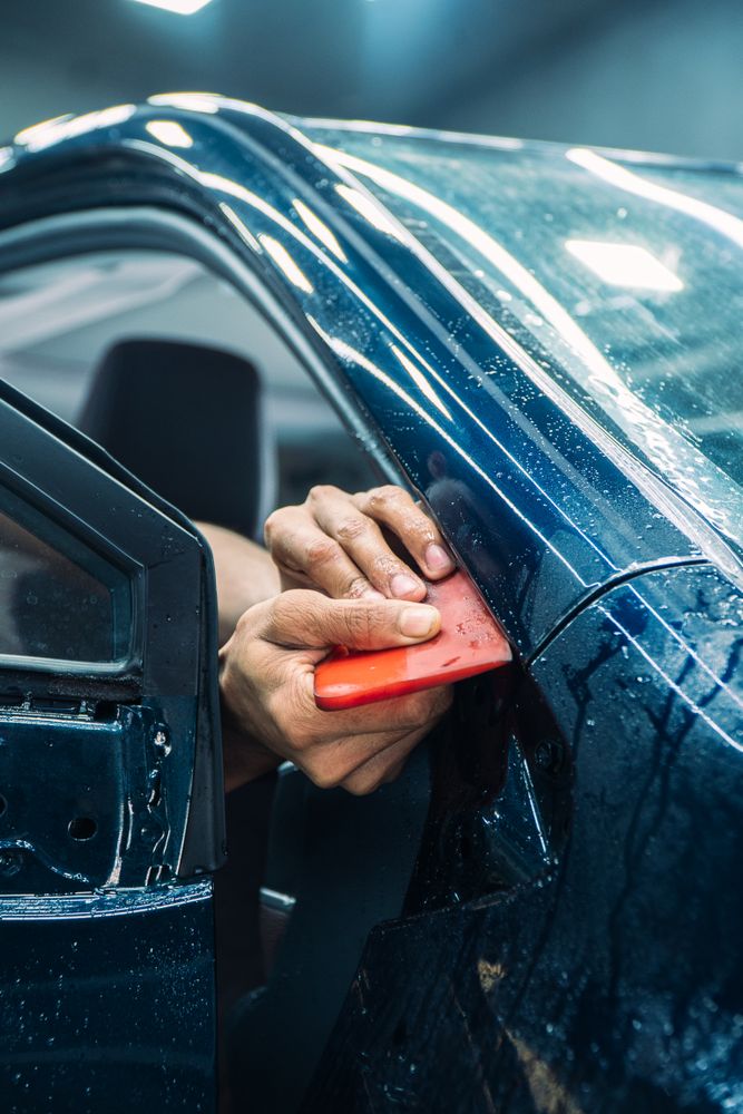 Technician applying clear paint protection film (PPF) to a car door in a workshop
