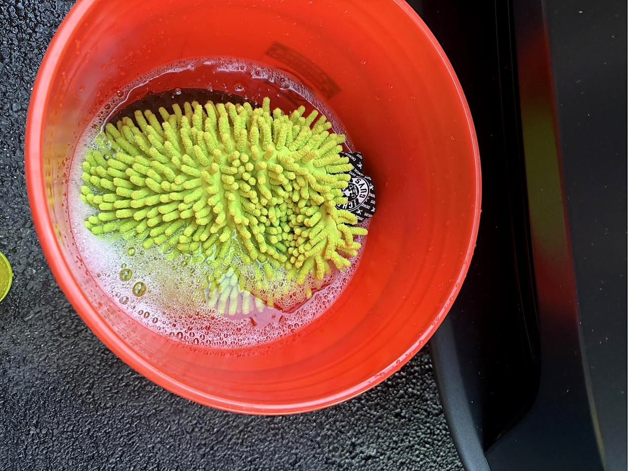 Green chenille wash mitt in a bucket of soapy water