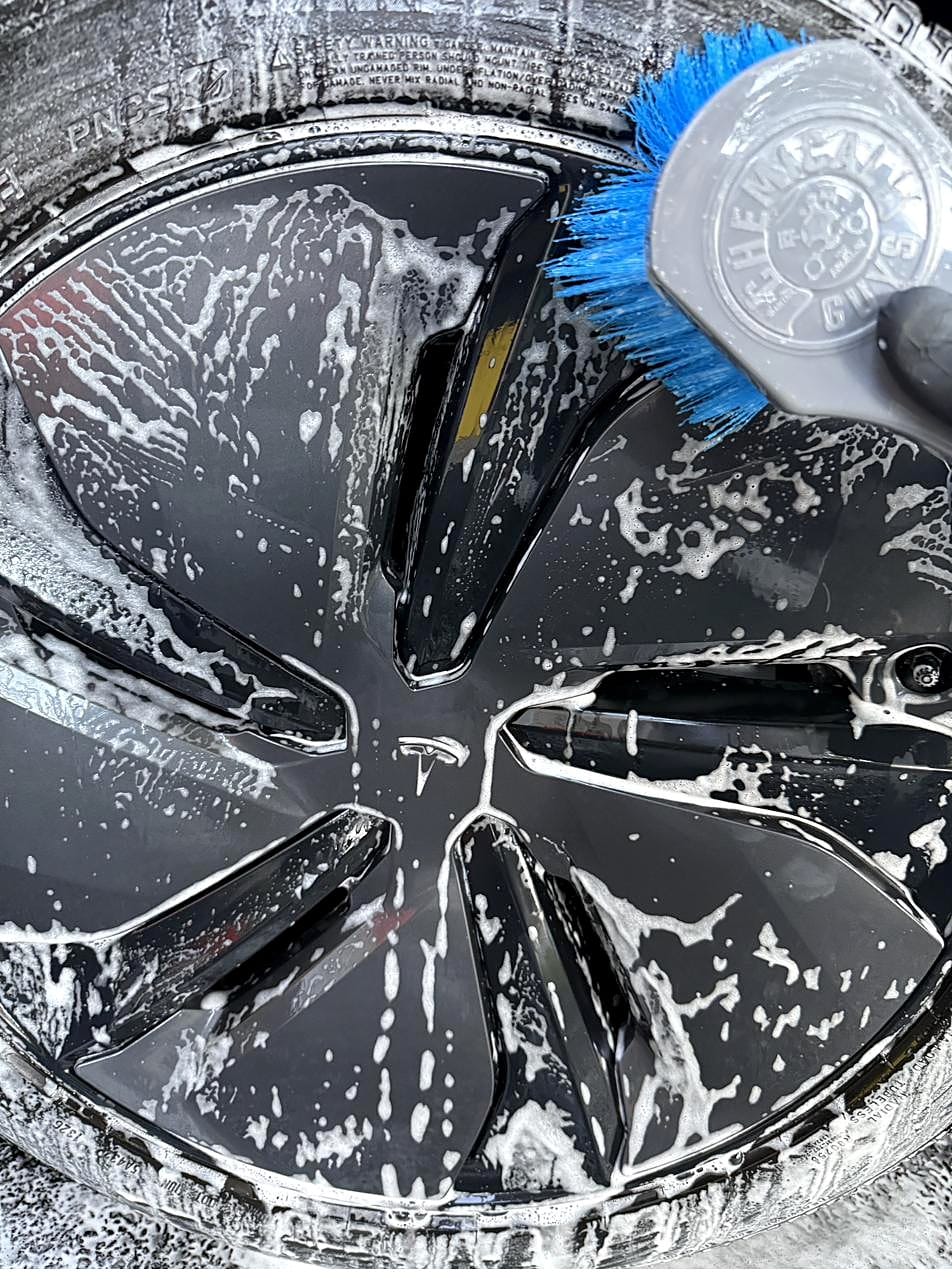 Scrubbing a Tesla Model Y wheel with a blue-bristle brush
